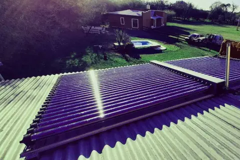 Colectores solares sobre un techo de chapa, con la pileta de una casa de campo al fondo