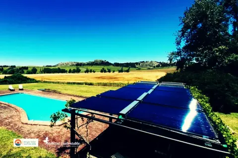 Colectores solares sobre una pérgola junto a una pileta, con el campo de fondo