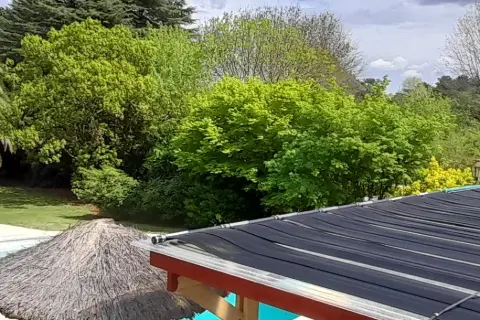 Colectores solares de pileta sobre un techo, entre árboles