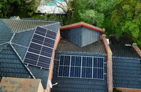 Casa con dos arreglos de paneles sobre tejas, vista aérea