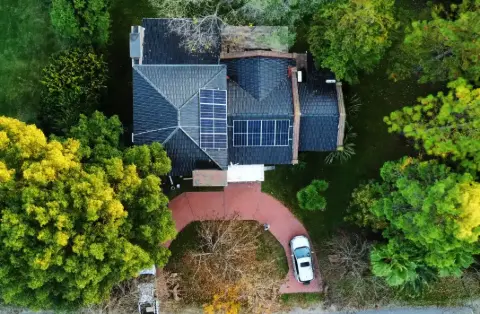 Vista aérea de una casa con paneles solares en el techo, rodeada de árboles
