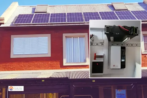 Paneles fotovoltaicos sobre el techo de una casa de ladrillo, con el inversor y las baterías en el recuadro