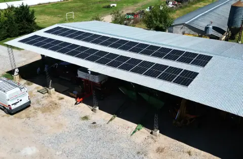 Dos filas de paneles solares sobre un galpón abierto, con una camioneta estacionada al costado