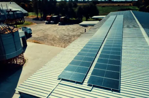 Dos filas de paneles solares sobre la cubierta de chapa de un galpón industrial, vista aérea